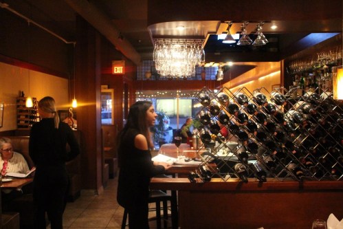 A cozy restaurant interior with a wine rack, dim lighting, and patrons enjoying their meals.