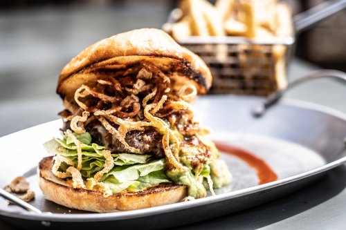 A gourmet burger with lettuce, crispy onions, and sauce, served on a metal plate with fries in the background.