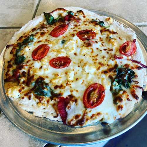 A freshly baked pizza topped with melted cheese, cherry tomatoes, and spinach on a silver platter.