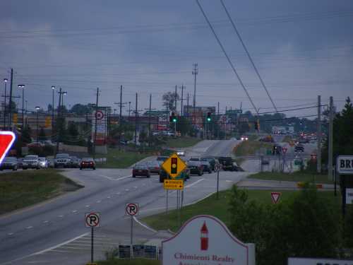 A busy intersection with traffic lights, cars, and commercial buildings under a cloudy sky.