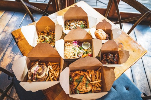 A table with various takeout boxes filled with burgers, fries, salads, and other dishes.