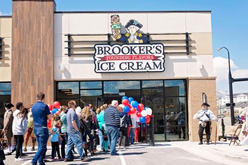 A crowd gathers outside Brooker's Ice Cream shop, decorated with balloons, for a grand opening event.