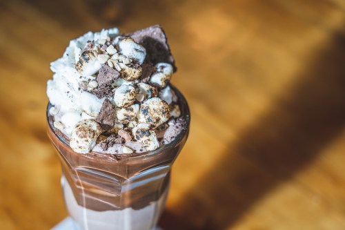 A tall glass filled with layers of chocolate, whipped cream, and topped with crushed cookies and marshmallows.