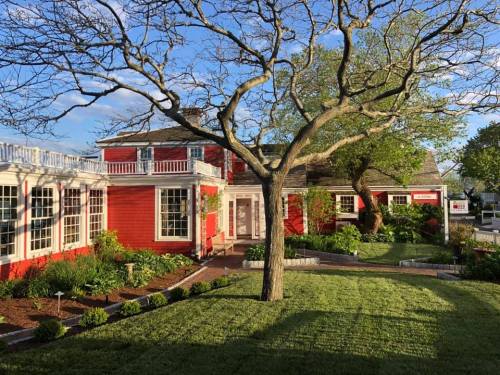 A charming red house with a large tree and well-maintained garden, bathed in warm sunlight.