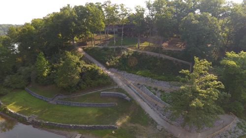 Aerial view of a park with a winding path, greenery, and a building in the background near a body of water.