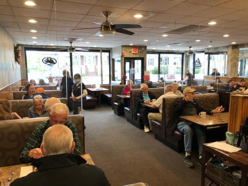 A busy diner with patrons seated in booths, chatting and enjoying meals, with a server attending to customers.