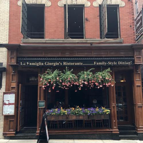 Exterior of La Famiglia Giorgio's Ristorante, featuring a wooden facade and vibrant flower baskets. Family-style dining sign visible.