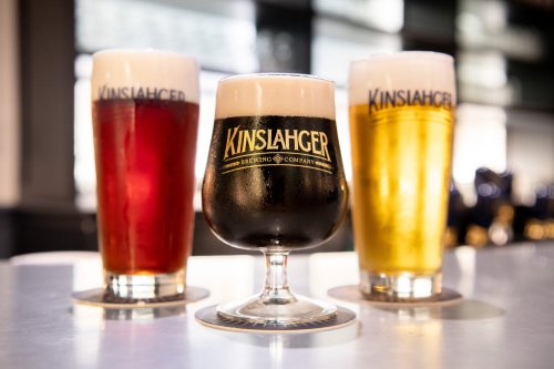 Three glasses of beer: a dark stout, a red ale, and a golden lager, all with frothy heads, on a bar counter.
