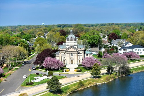 Aerial view of a historic building surrounded by blooming trees and a serene waterfront in a suburban area.