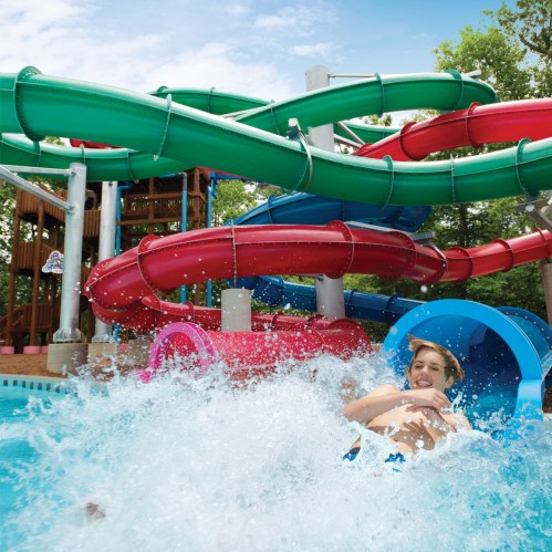 A child joyfully splashes into a pool from a colorful water slide on a sunny day.