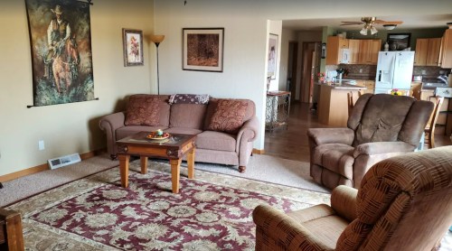 Cozy living room with two sofas, a coffee table, and a patterned rug, leading to a kitchen area in the background.