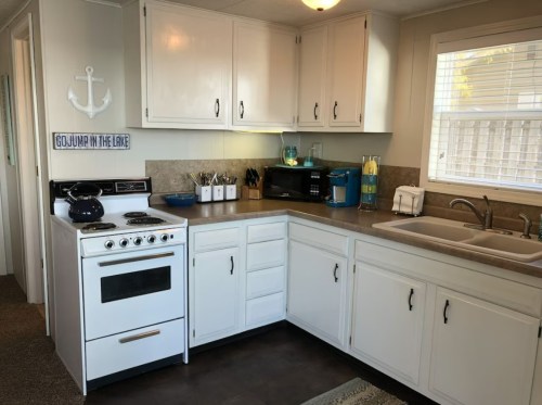 Bright kitchen with white cabinets, a stove, sink, and countertop appliances, featuring a cozy, inviting atmosphere.