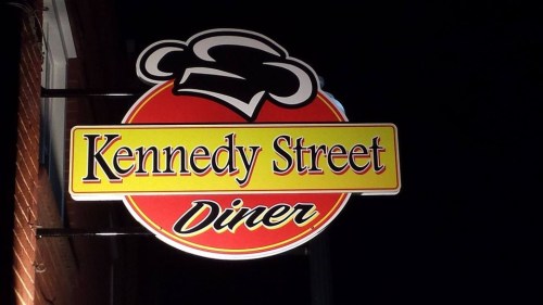 Sign for Kennedy Street Diner featuring a chef's hat graphic, illuminated against a dark background.