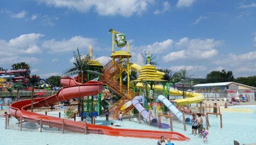 Colorful water slides and attractions at a water park, with families enjoying the pool under a blue sky.