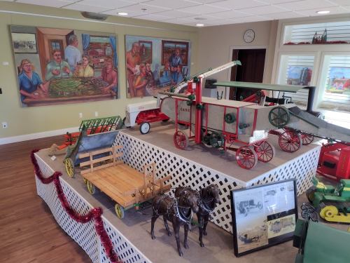 A display of vintage toys and models, including a plane and farm equipment, set against colorful murals.