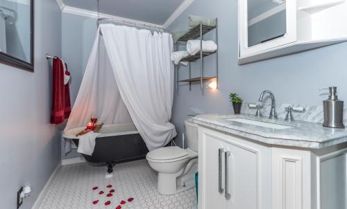 A cozy bathroom featuring a clawfoot tub, white shower curtain, and rose petals on the floor, with modern fixtures.