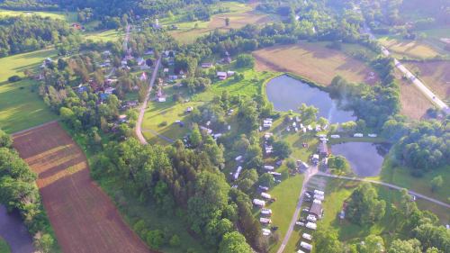 Aerial view of a rural landscape with a pond, green fields, and scattered houses and RVs among trees.