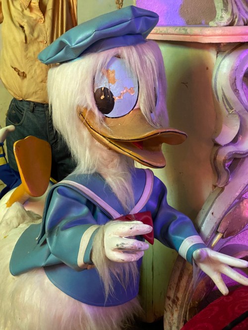 A whimsical, vintage duck character in a blue outfit with a large head and exaggerated features, set against a colorful background.