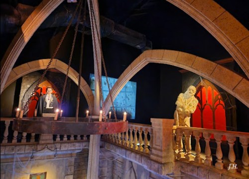 A dimly lit room with stone arches, featuring two eerie figures and a chandelier with candles.