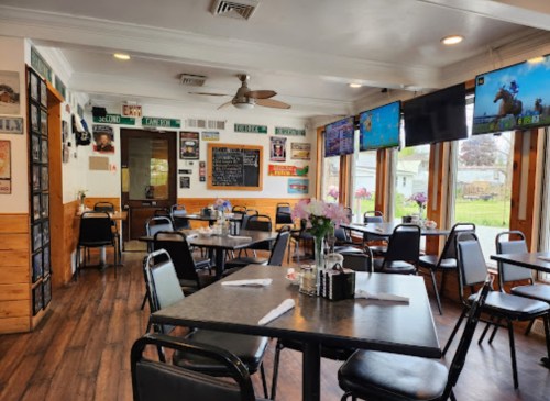 Cozy restaurant interior with black chairs, tables, and large windows, featuring decor and TVs on the walls.