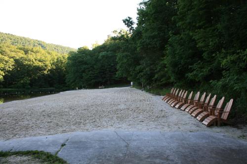 A sandy beach area with wooden chairs lined up, surrounded by lush green trees and a calm water body.