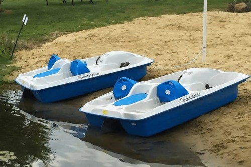 Two blue and white paddle boats on a sandy shore next to a calm body of water.