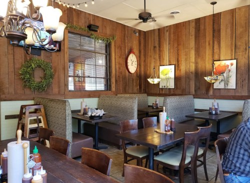 Cozy restaurant interior with wooden walls, booths, tables, and decorative plants and artwork.