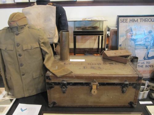 A vintage military uniform and trunk displayed in a museum, showcasing historical artifacts from the early 20th century.