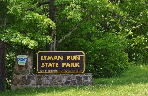Sign for Lyman Run State Park surrounded by lush green trees and grass.