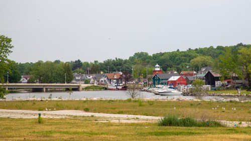 A scenic view of a harbor with boats, colorful buildings, and greenery under a cloudy sky.