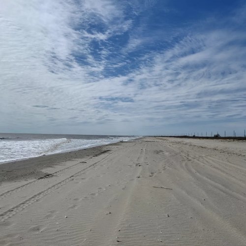 A sandy beach stretches towards the horizon under a cloudy sky, with gentle waves lapping at the shore.