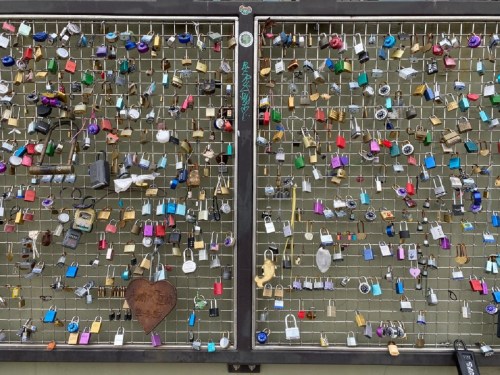 A metal grid covered with various colorful padlocks of different shapes and sizes.