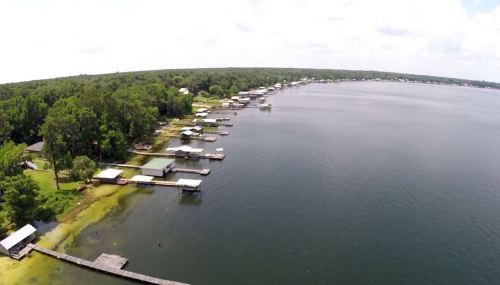 Aerial view of a calm lake with docks and houses along the shoreline, surrounded by lush greenery.