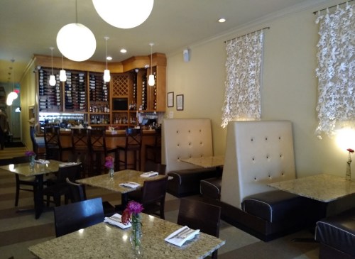 Cozy restaurant interior with booths, tables, and a bar area, featuring soft lighting and floral centerpieces.