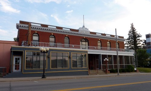 Historic brick building with large windows and a balcony, featuring a decorative roof and street lamps in front.