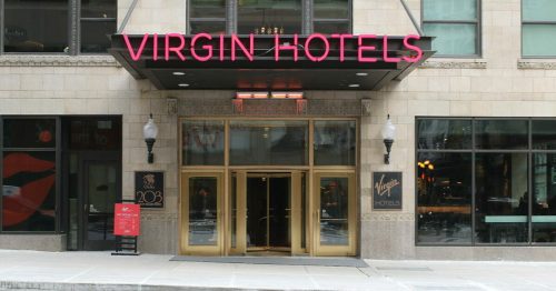 Entrance of Virgin Hotels with large glass doors and a neon sign, located in an urban setting.