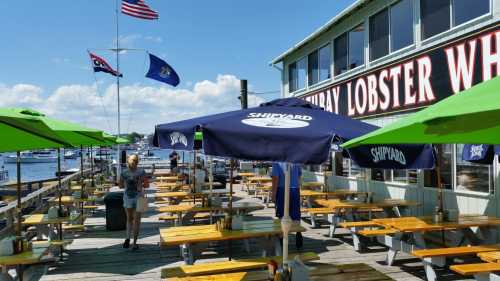 Outdoor dining area at a seafood restaurant with green umbrellas, flags, and a view of the harbor.