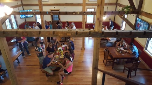 A busy restaurant interior with wooden beams, tables filled with diners, and a lively atmosphere.