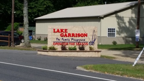 Sign for Lake Garrison, "The Family Playground," indicating it is open for the season, with a building in the background.