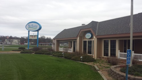 Exterior view of The Rivers Family Restaurant, featuring a sign and landscaped grounds on a cloudy day.