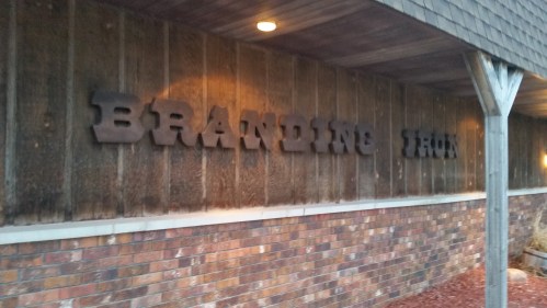 Sign on a rustic wall displaying the words "BRANDING IRON" in bold, metal letters.