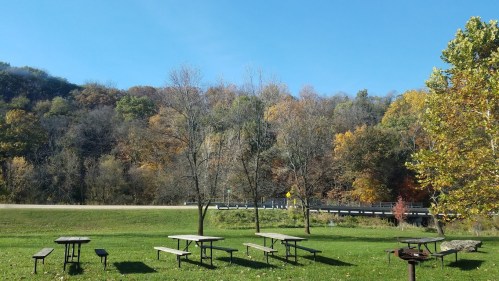 A serene park scene with picnic tables, colorful autumn trees, and a clear blue sky.