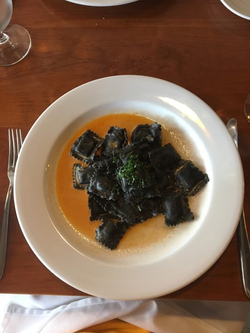 A plate of black ravioli topped with a light sauce and garnished with parsley, served on a wooden table.