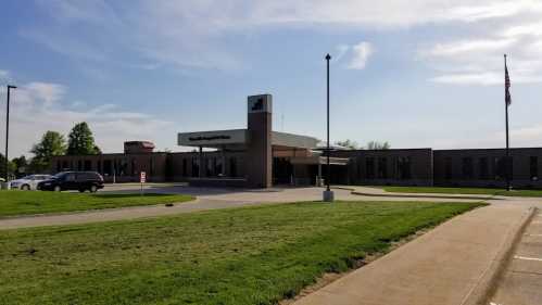 A modern building with a flat roof, surrounded by green grass and a clear sky, likely a public facility or office.