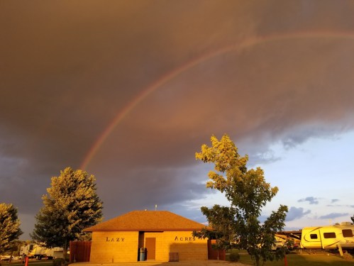A rainbow arcs over a building labeled "Lazy Acres" with dark clouds and trees in the foreground.