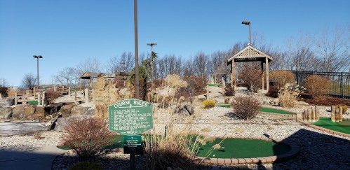 A mini-golf course with landscaped areas, rocks, and a gazebo under a clear blue sky.
