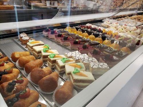 A display case filled with various colorful pastries and desserts, including cakes, tarts, and cream-filled treats.