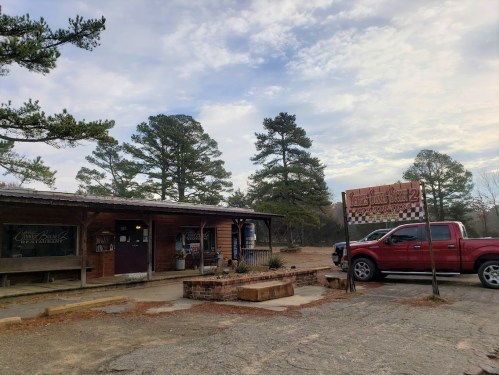 A rustic building with a red truck parked outside, surrounded by trees and a sign for a restaurant.