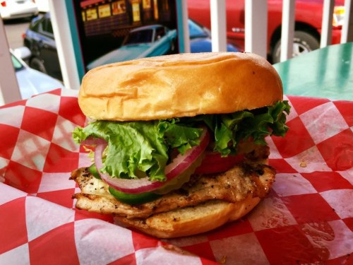 A grilled chicken sandwich with lettuce, tomato, and onion on a toasted bun, served in a red and white checkered wrapper.