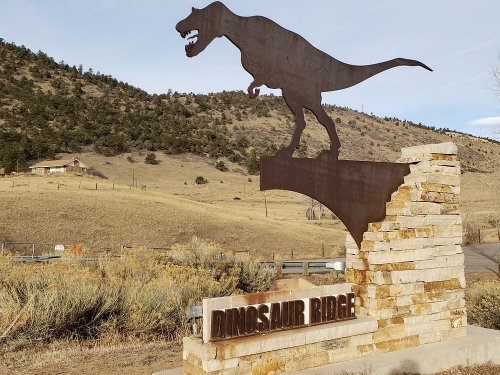Sign for Dinosaur Ridge featuring a silhouette of a dinosaur against a hilly landscape.